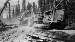 A black dozer operator driving a dozer hauling a carryall over a culvert. 1942