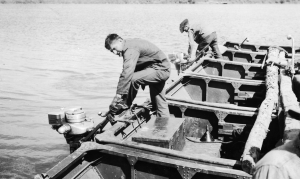 Two soldiers of 73rd Pontoon Engineers starting outboard motors to propel the Teslin Pontoon Ferry. 1942