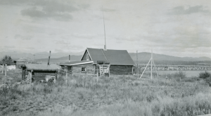 A local native log cabin with original wood Teslin River Bridge, Johnsons Crossing, in background.1942
