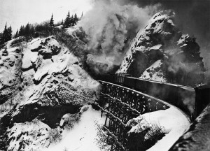 Train travelling over wooden bridge through a tunnel on its way over White Pass. 1942